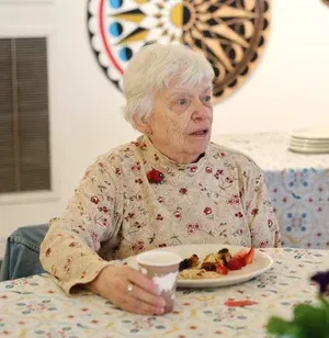 Person seated at a table with a plate of food and a cup in a cozy dining room