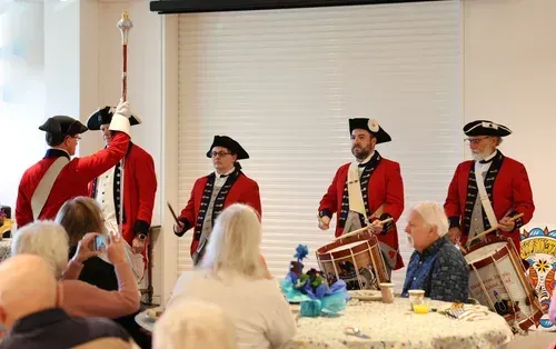 Colonial reenactors in red coats perform for an audience at an indoor event