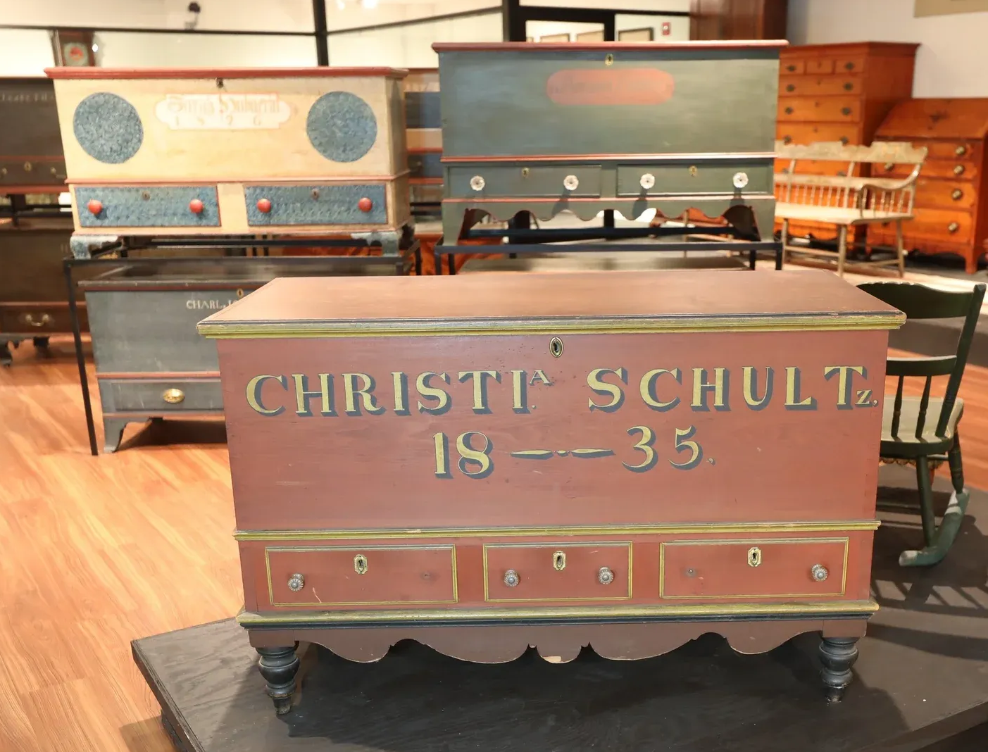 Vintage painted wooden chest reading “Christi Schultz IS-35” in a room with antique furniture.