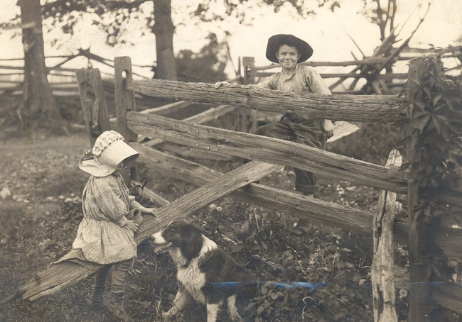 Two children and a dog by a wooden fence in a rural yard, vintage sepia photo