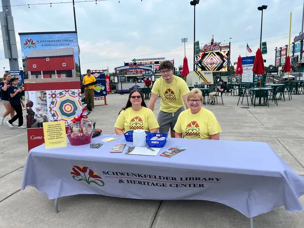 Three volunteers at a community fair table with a sign for McKinleyville Library.