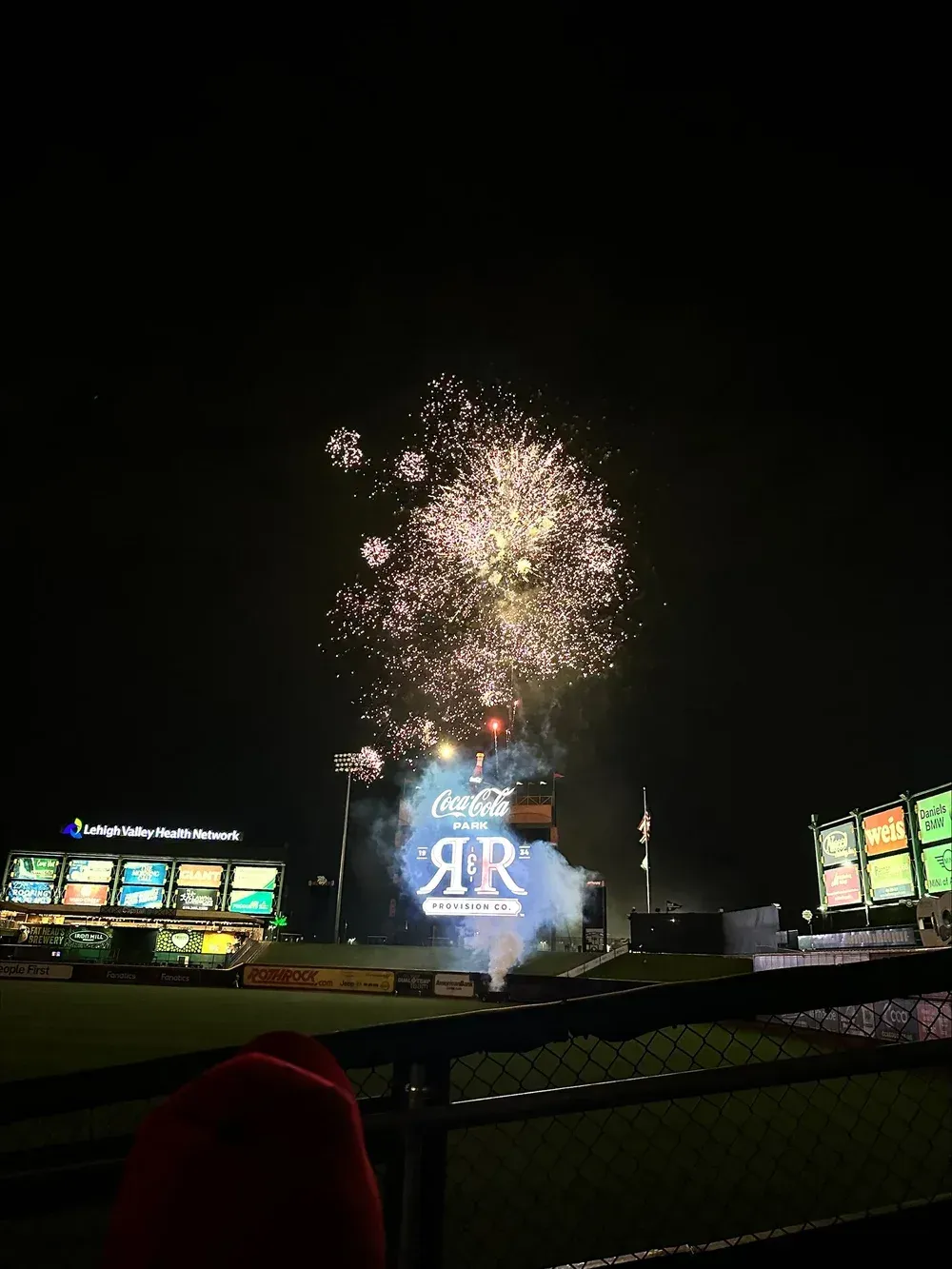 Fireworks burst above a lit stadium scoreboard at night, with a large “RR” logo below.