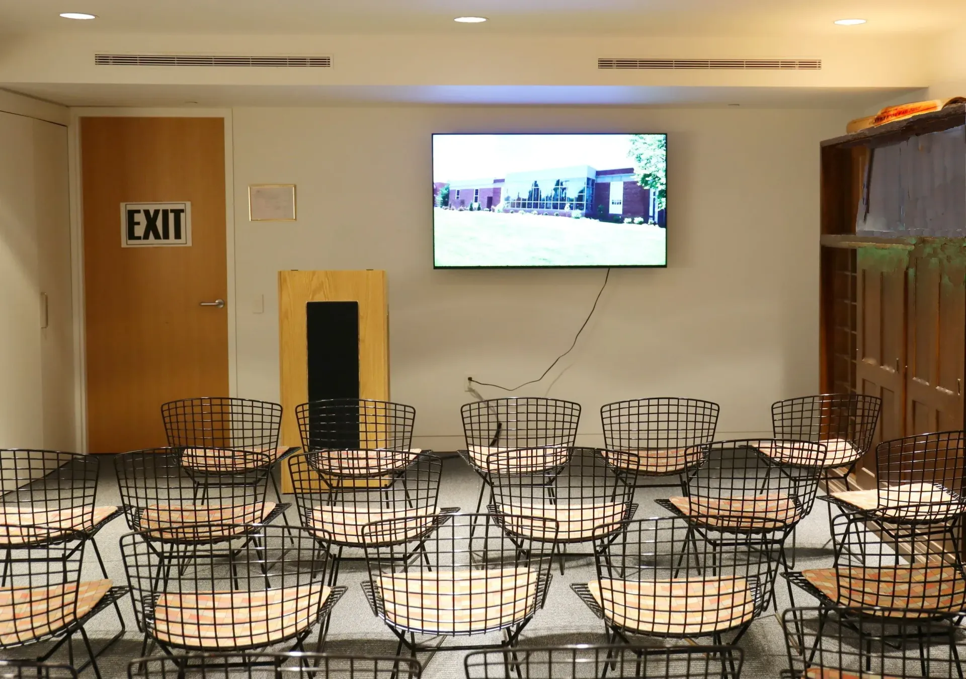 Empty banquet room with rows of chairs and round tables, wall-mounted TV, and exit door
