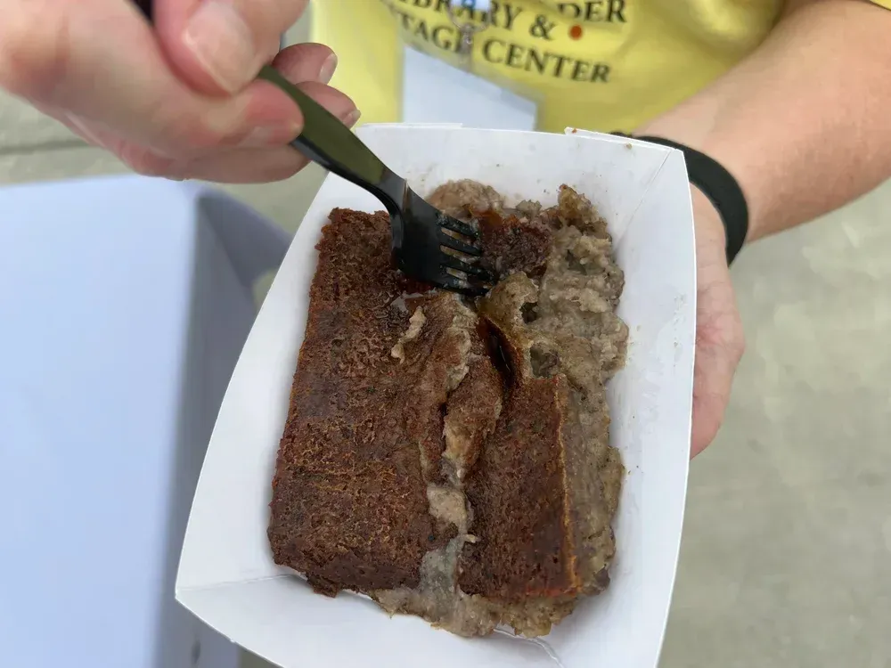 Person eating a brown dessert with a fork from a white takeout container