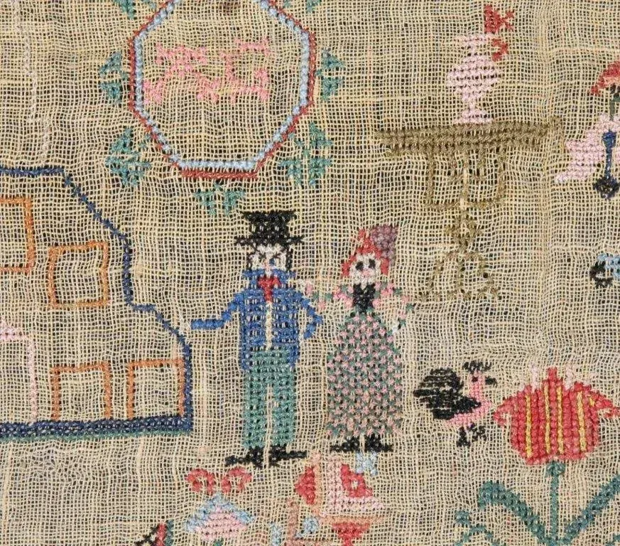 Embroidered figures in blue and tan stand on a woven fabric background with colorful stitched patterns.