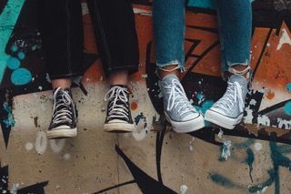 Four pairs of sneakers hanging by their toes against a colorful graffiti wall.