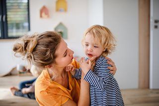 Woman in orange shirt holding a child in a striped shirt indoors