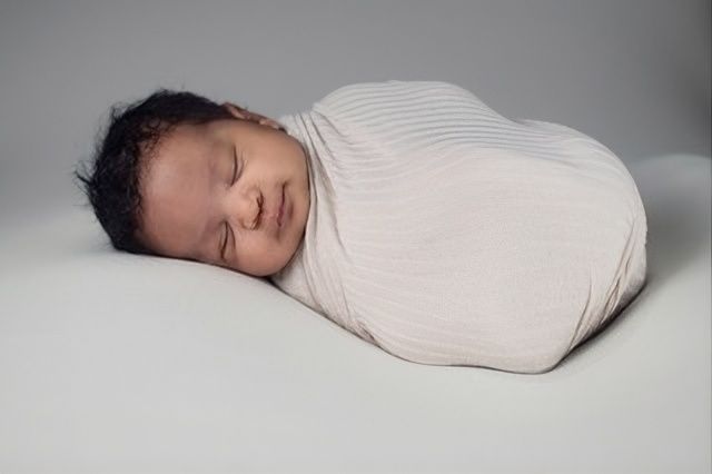 Sleeping newborn swaddled in a white blanket on a gray surface