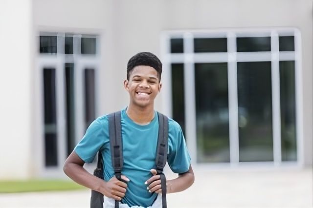 Smiling student in a teal shirt with a backpack standing outside a building