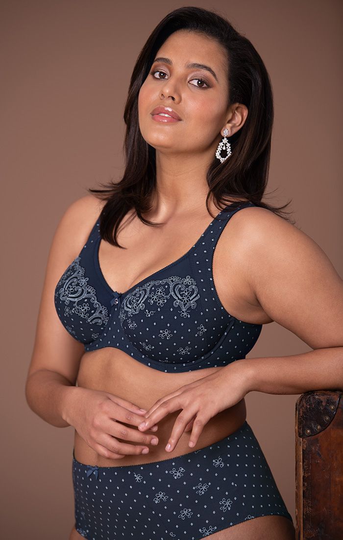 Woman in a navy patterned outfit poses against a plain brown backdrop.