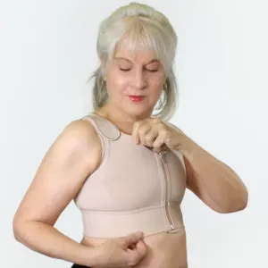 Woman in a beige sports bra adjusting the front zipper against a plain white background