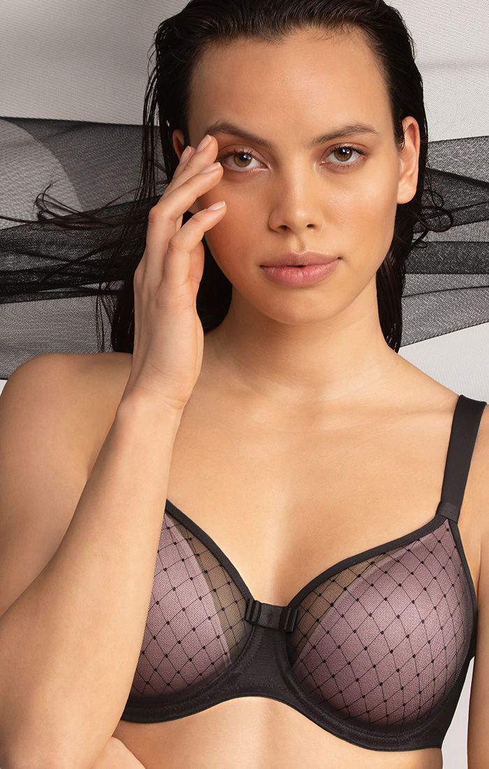 Woman posing in a black lace bra with sheer black fabric backdrop, looking at the camera.