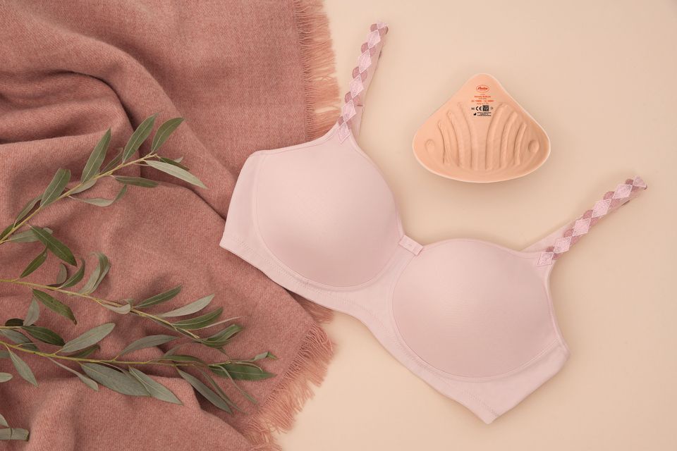 Pink bra with matching underwear and folded fabric on a beige background with leaves