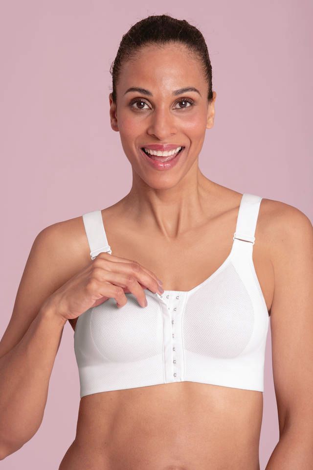 Woman in white sports bra smiling against a pink background, holding the front clasp
