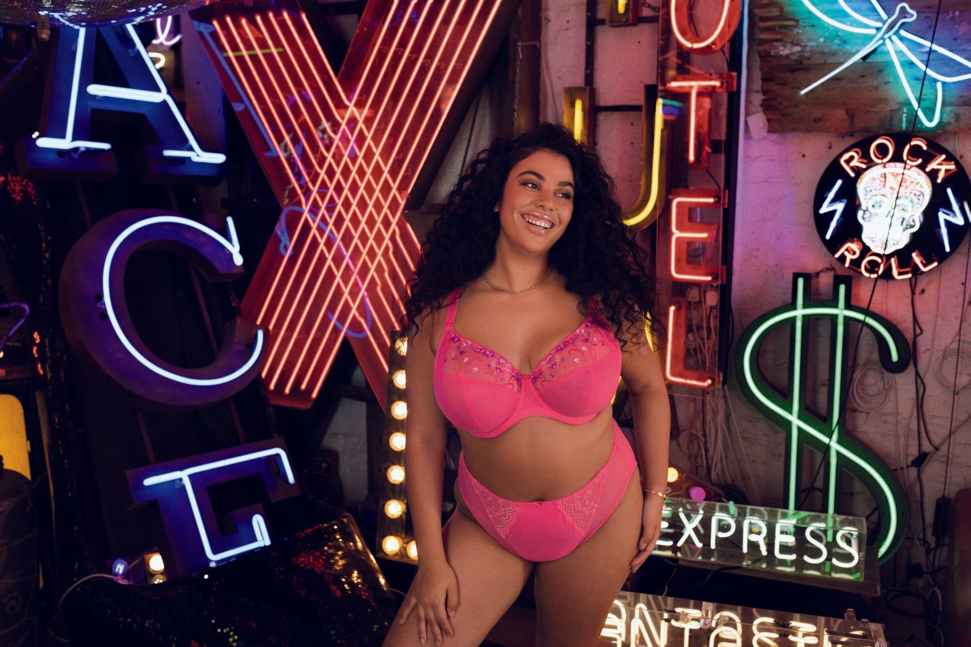 Woman in pink lingerie posing amid neon signs and colorful lights in a nightclub-style setting