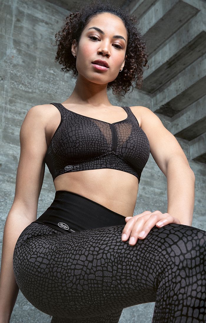 Woman in black athletic wear posing in a low-angle urban setting, with a concrete stairwell behind her.