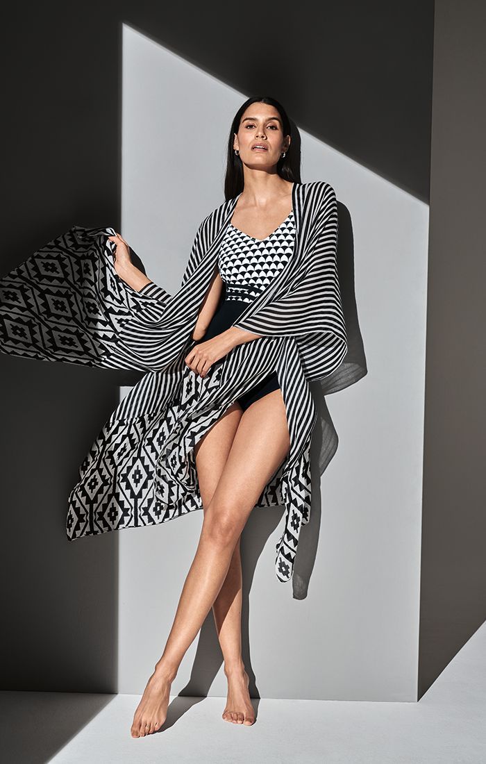 Fashion model in a black-and-white patterned outfit posing against a geometric gray backdrop.
