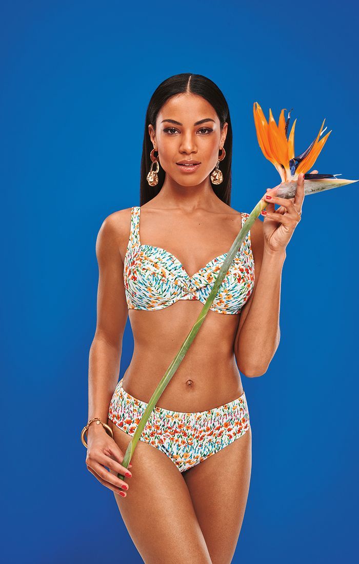 Woman in floral bikini holding an orange bird of paradise flower against a blue background.