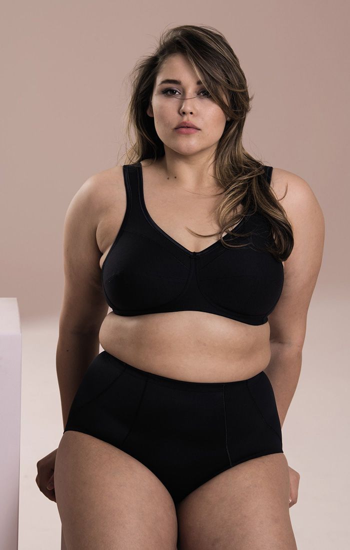 Person in black sports bra and high-waisted shorts against a soft pink background.