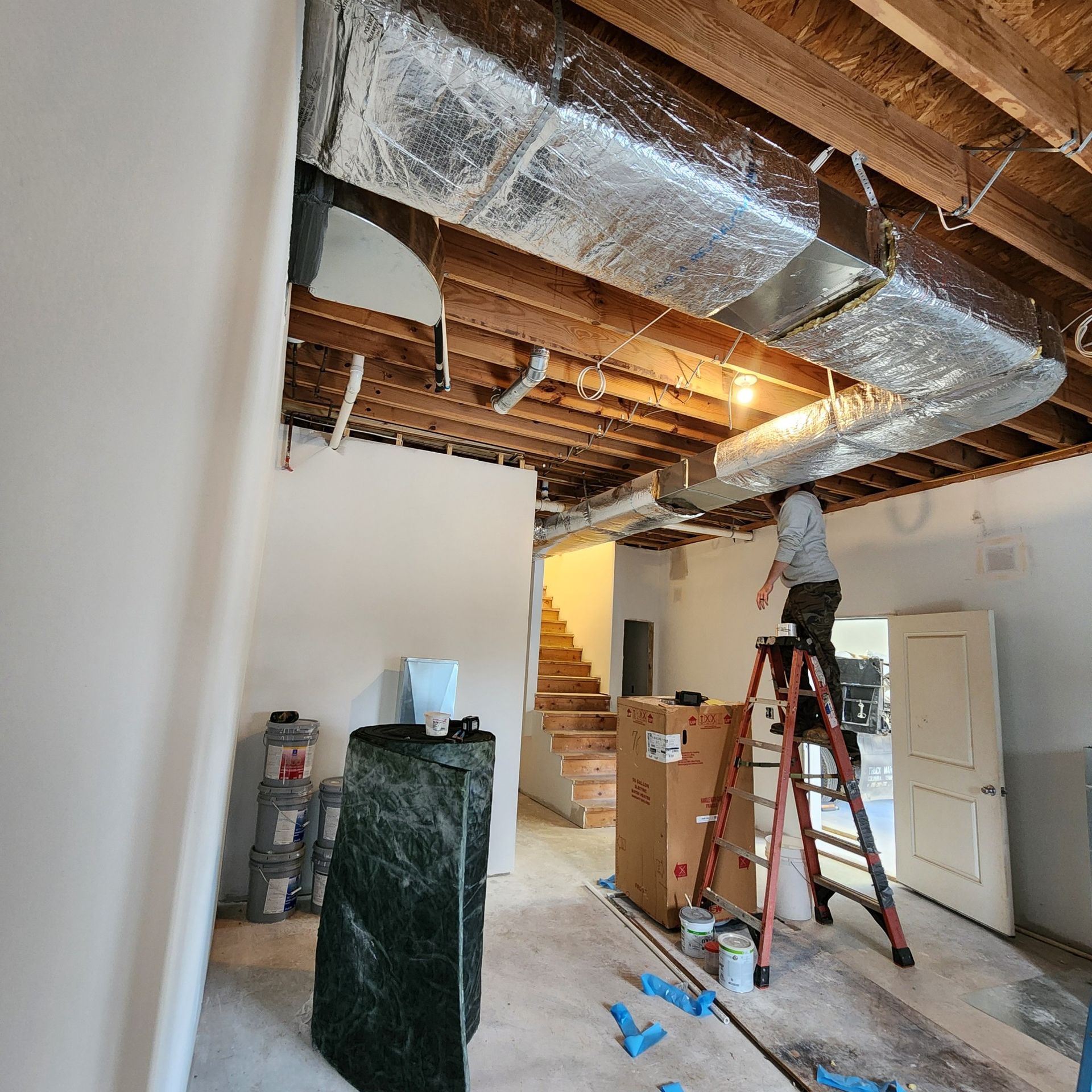 Person on a ladder working on ductwork in a room under construction.
