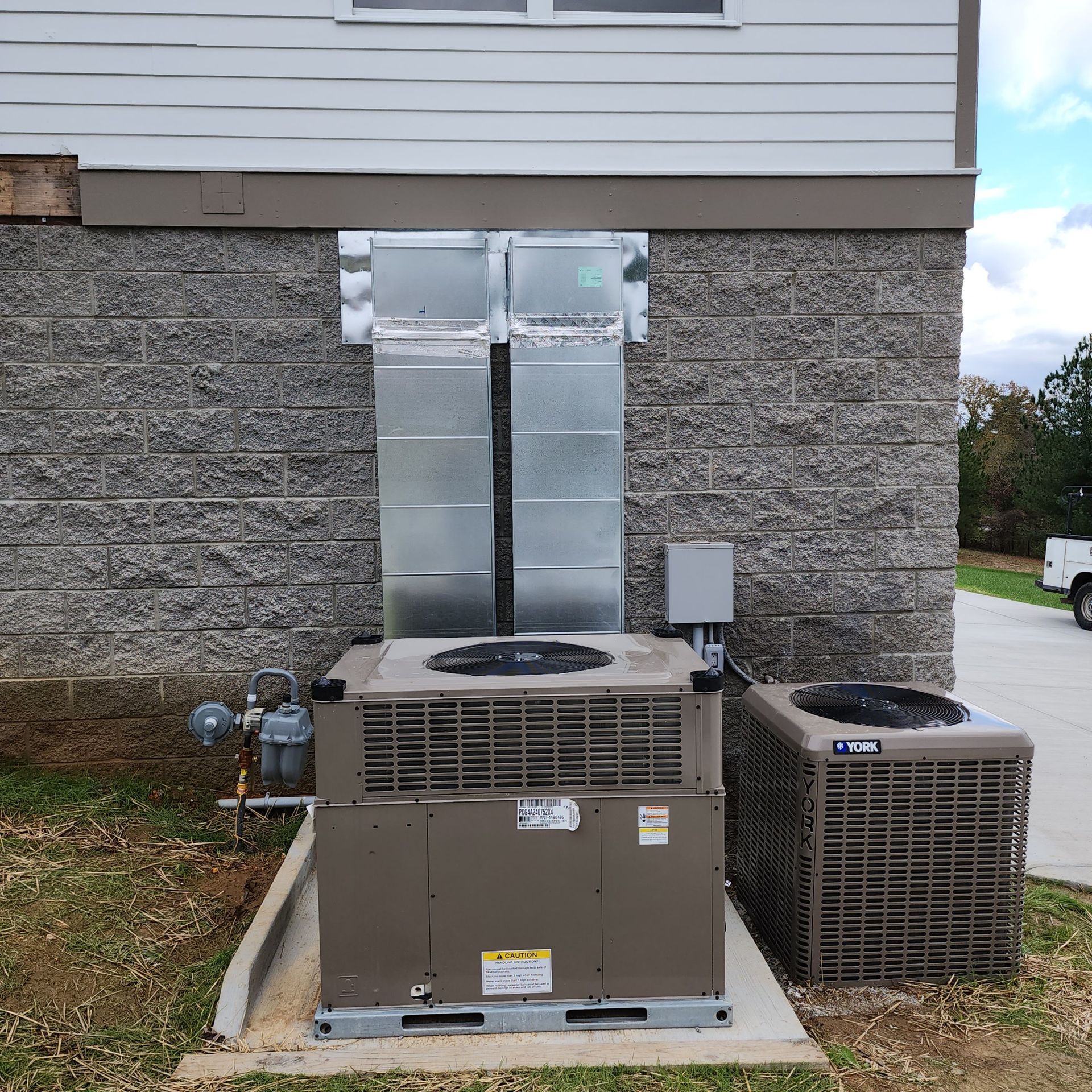 Two HVAC units with ductwork attached to a building's exterior wall.