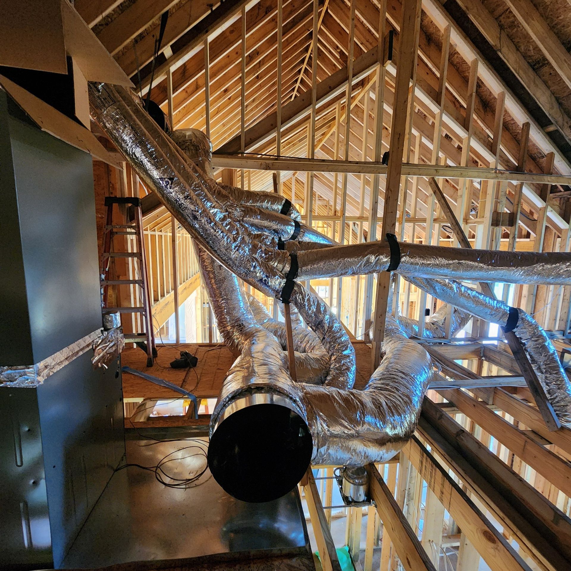 HVAC ductwork installation in an unfinished attic with wooden framing and a black vent.