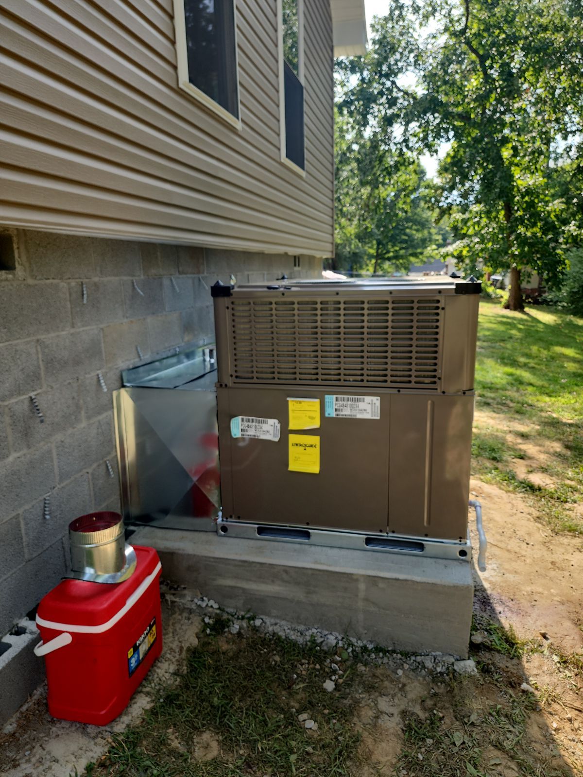 Air conditioning unit next to a house with a red cooler and metal ductwork.