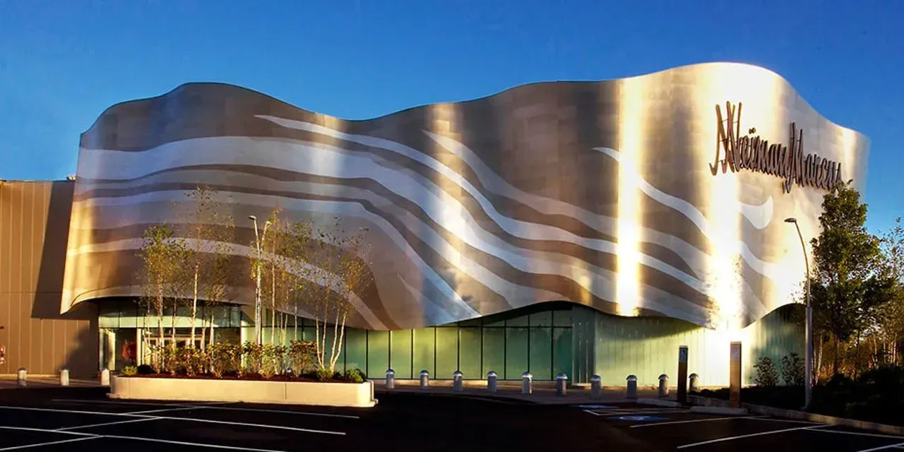 Curved modern building with gold and silver wavy facade at dusk, lit by warm exterior lights.