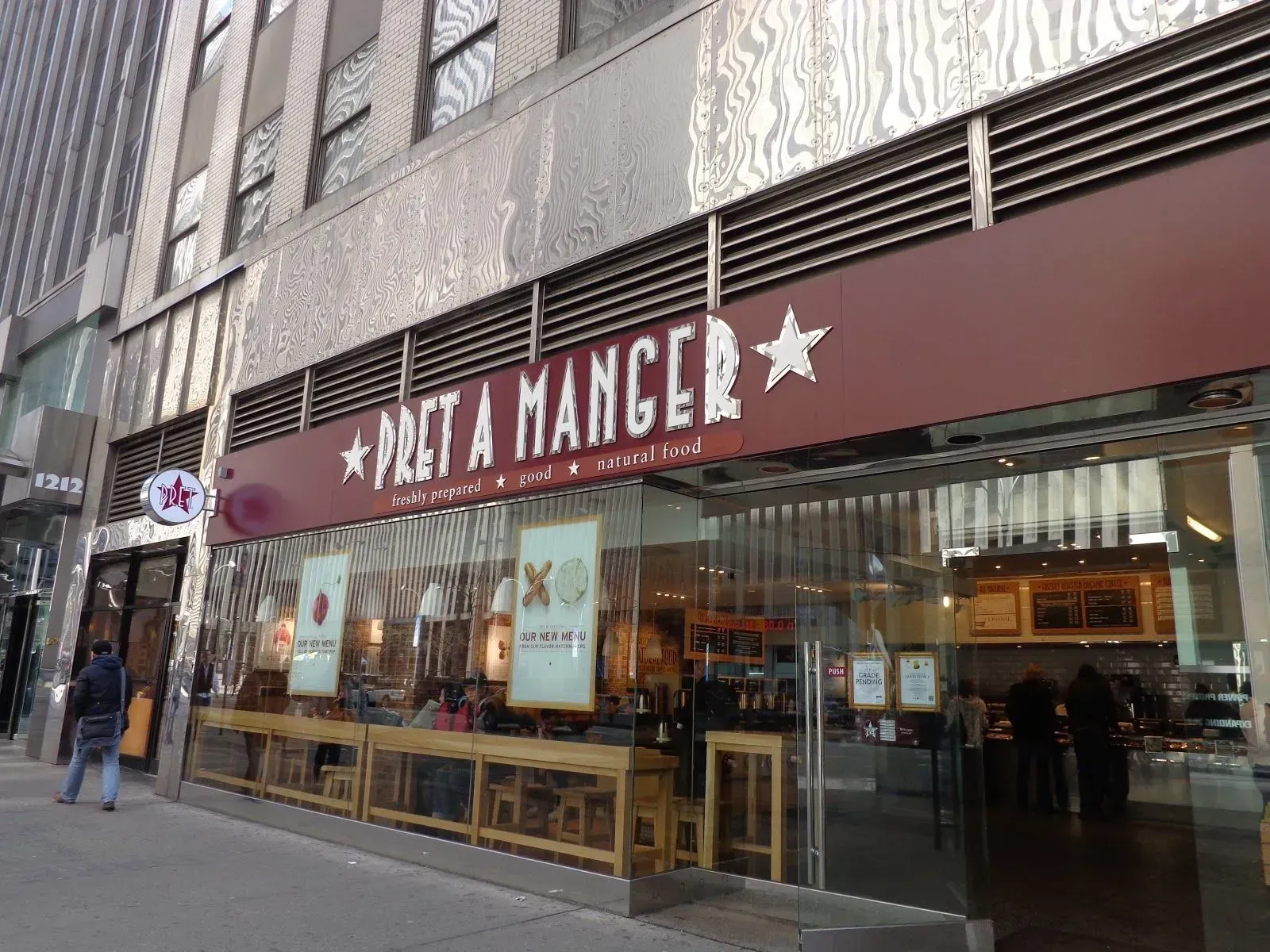 Street-level storefront with a maroon “Milananger” sign and large glass windows on a city sidewalk.
