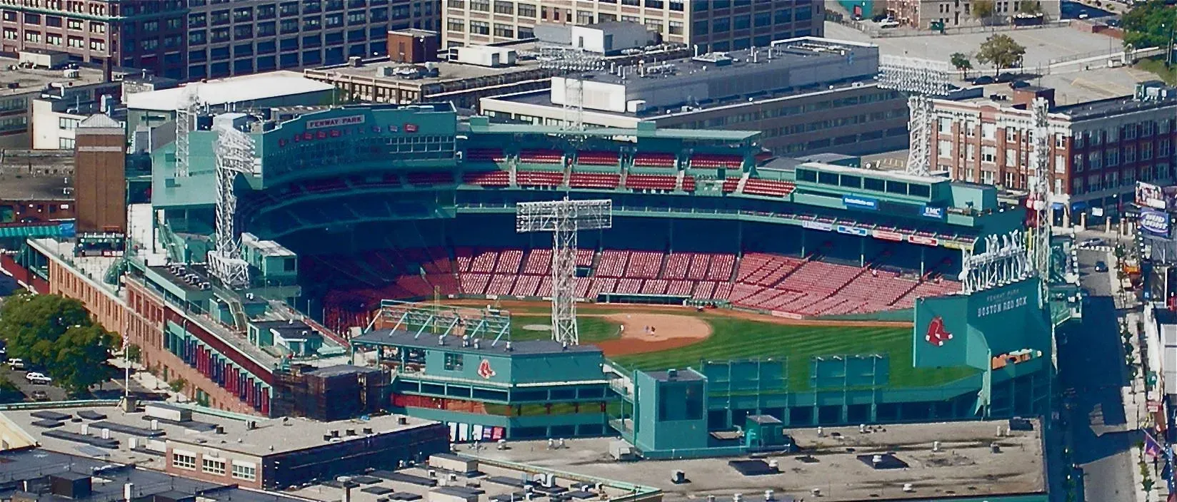 Aerial view of a baseball stadium with a green field and red seats in an urban area