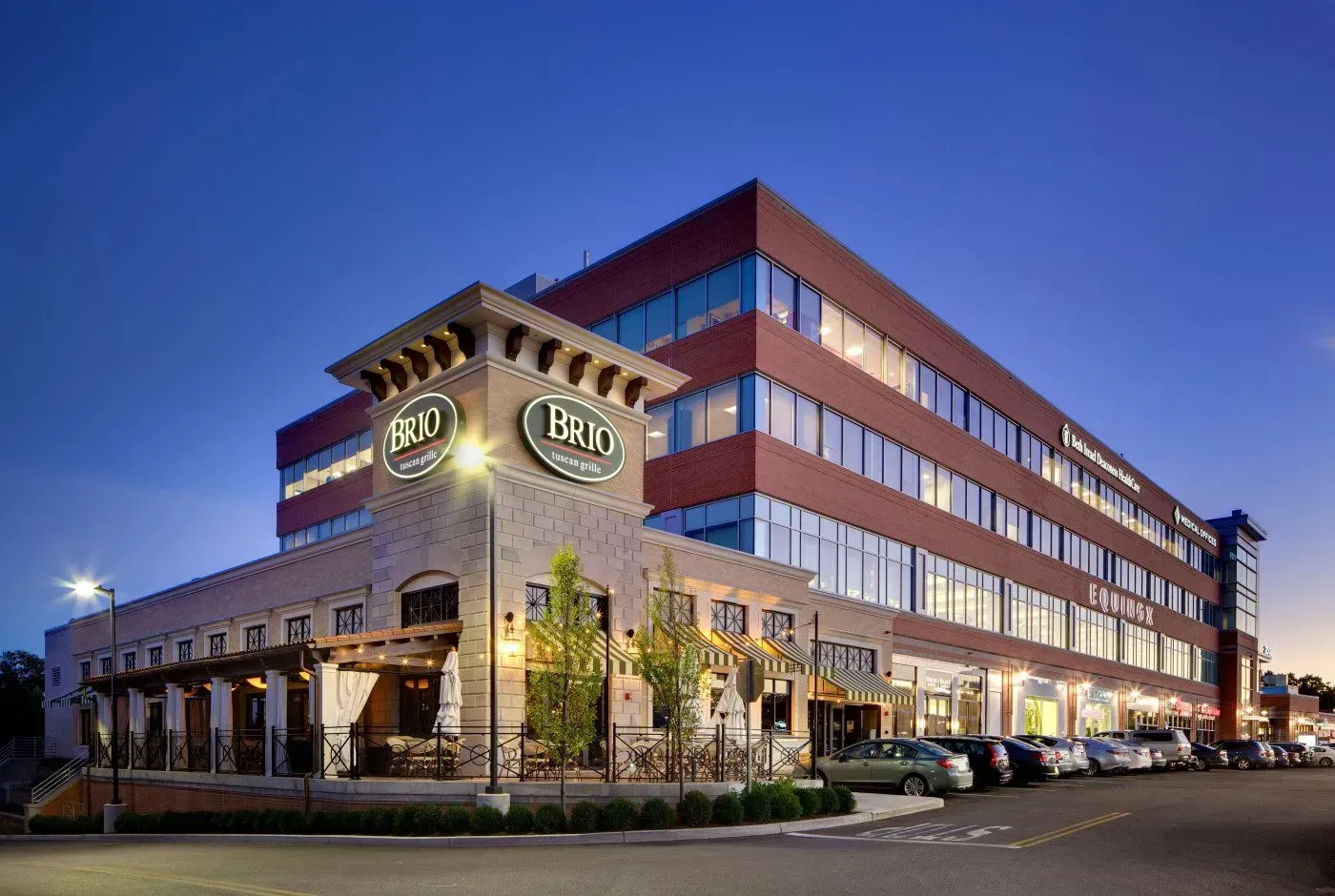Brick hotel exterior at dusk with lit windows, arched entrance, and parked cars