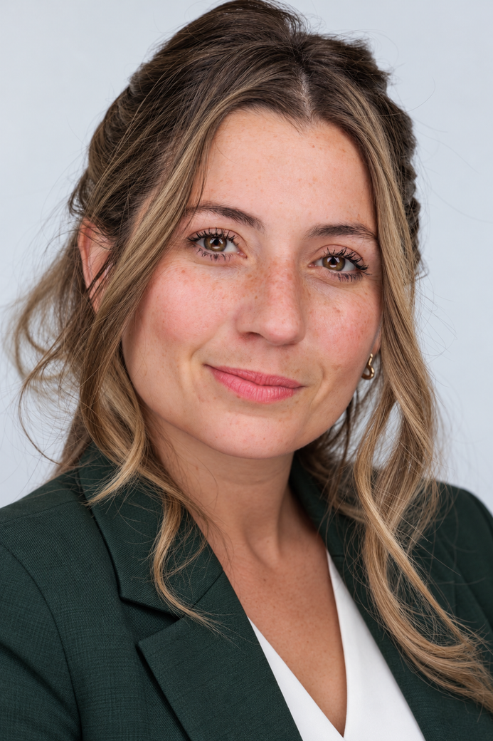 Portrait of a woman in a dark green blazer, softly smiling against a light gray background