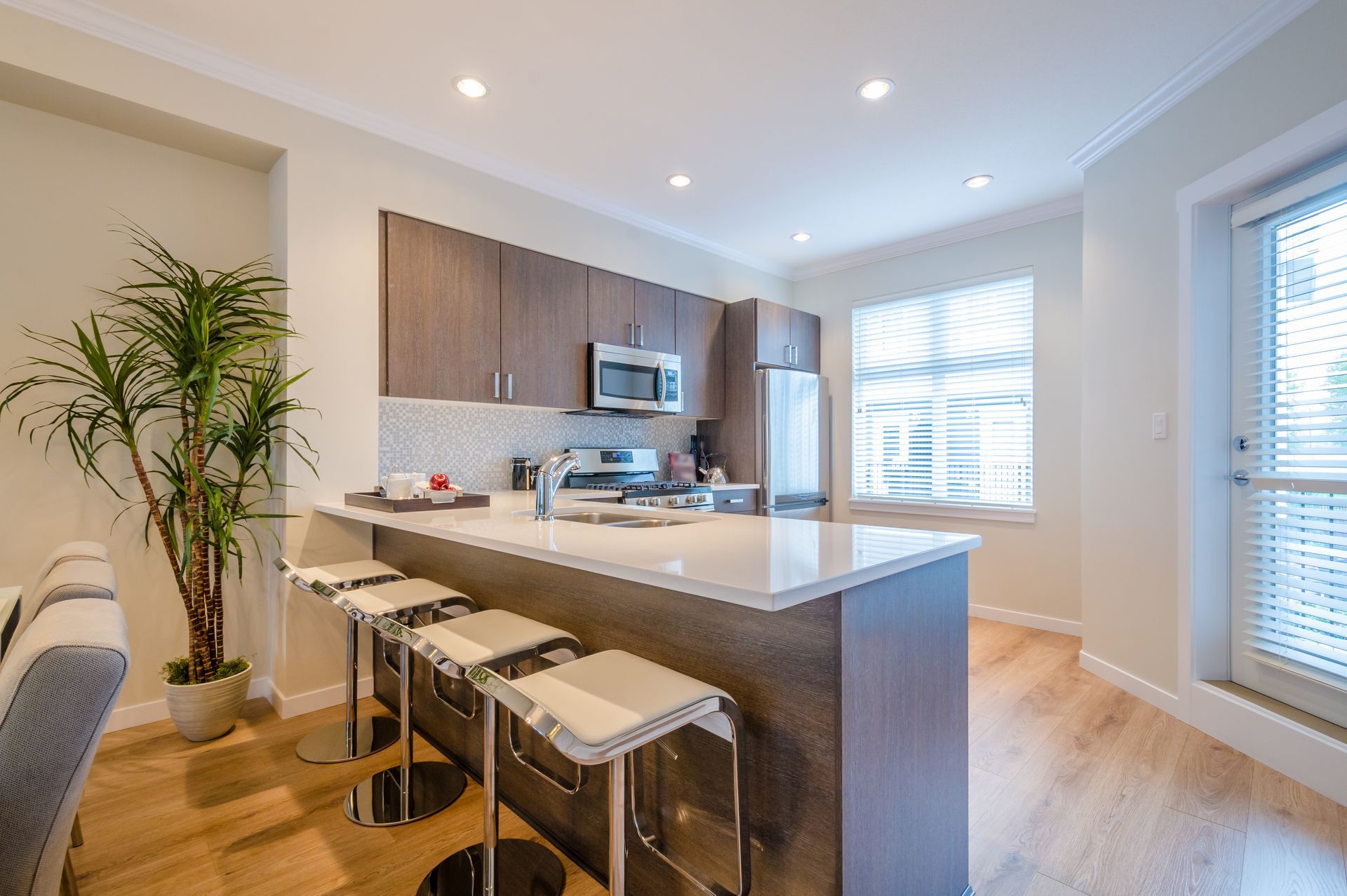 Compact kitchen with flat-front wood cabinets, a white peninsula, and three bar stools.