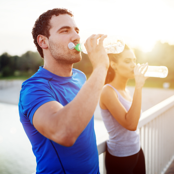 A man in a blue shirt is drinking water from a bottle