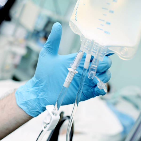 A person wearing a blue glove is holding an iv bag