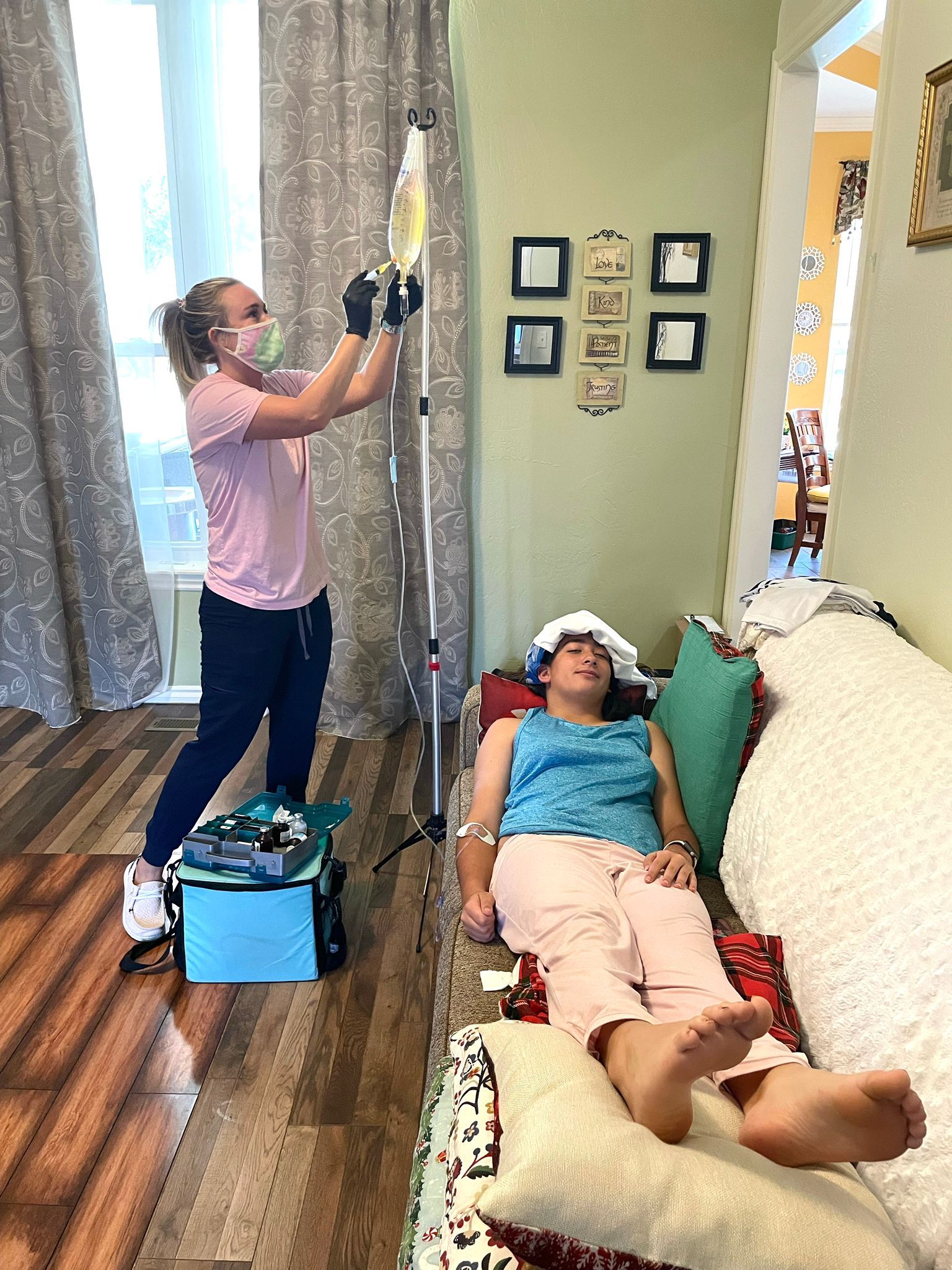 A woman is giving an iv to a woman laying on a couch.