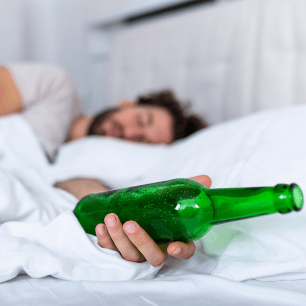 A man is laying in bed holding a green bottle of beer.