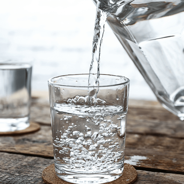 Water is being poured into a glass on a wooden table.