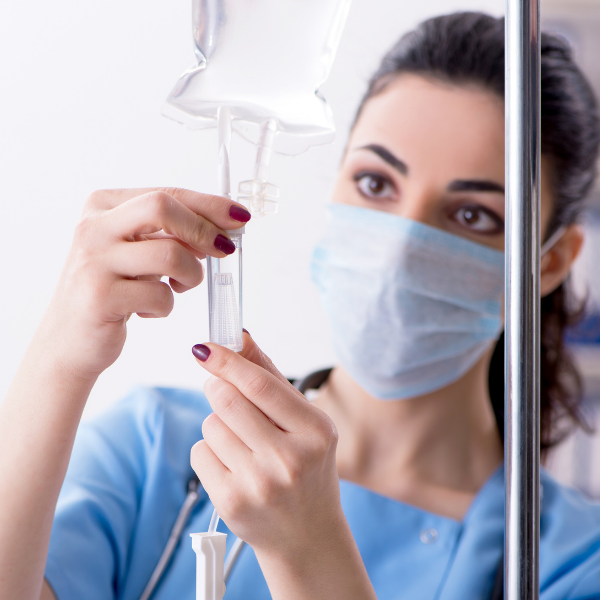 A nurse wearing a mask is preparing an intravenous drip.