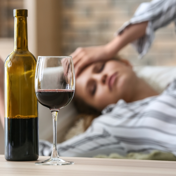 A woman is laying on a bed next to a bottle of wine and a glass of wine.