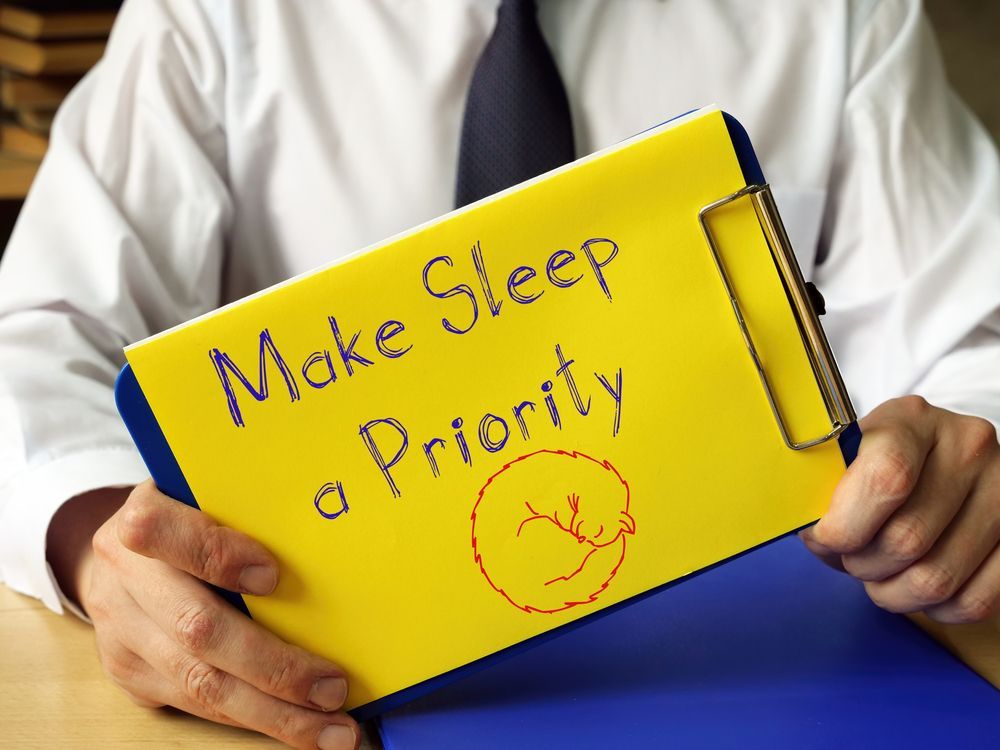 A man is holding a clipboard that says make sleep a priority
