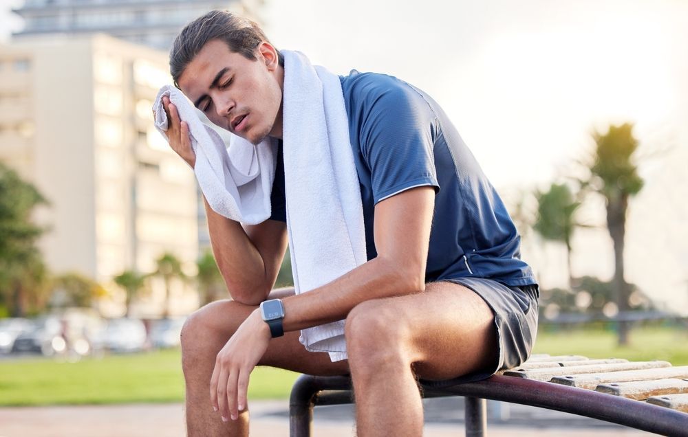 A man is sitting on a bench with a towel around his neck.
