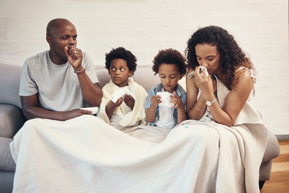 A family is sitting on a couch under a blanket.