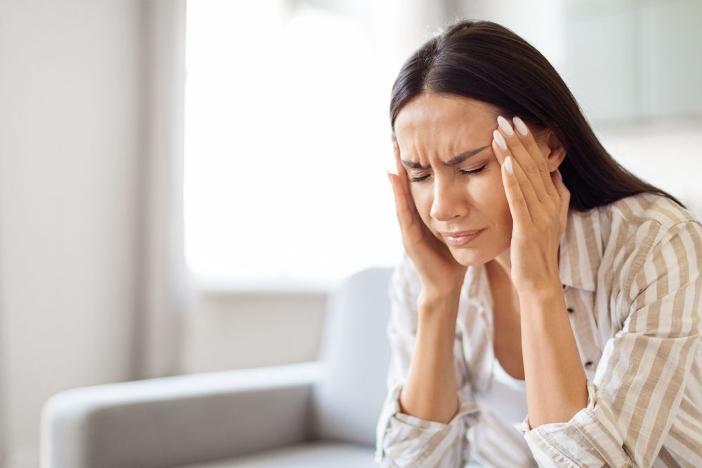 A woman is sitting on a couch with her hands on her head.