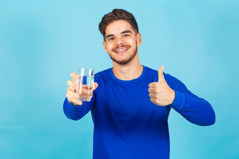 A man in a blue shirt is holding a glass of water and giving a thumbs up.