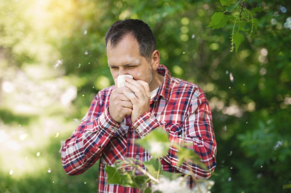 A man in a plaid shirt is blowing his nose in a park.