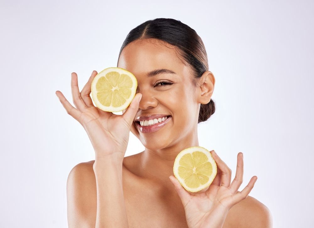 A woman is holding two slices of lemon in front of her eyes.