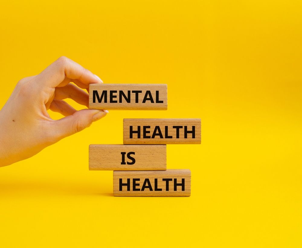 A hand is holding a wooden block with the words `` mental health is health '' written on it.