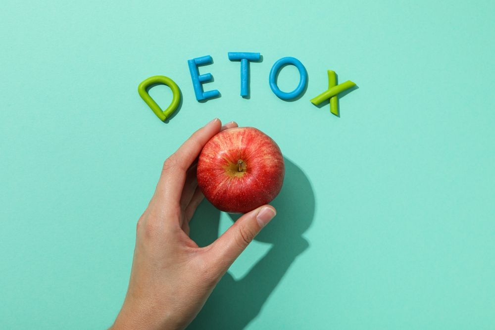 A hand is holding an apple in front of the word detox.