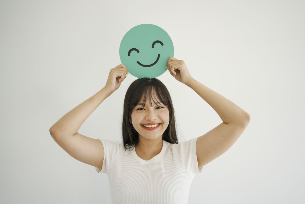 A woman is holding a paper smiley face over her head.
